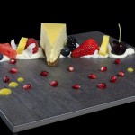 Best Cheesecake Recipes A photo of a slice of Mango Cheesecake plated on a black slate tile with Mascarpone Cream and Fruit salad.