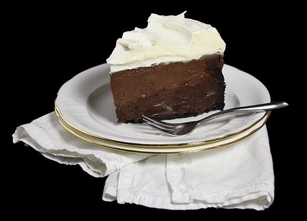 Mud Cake A close up photo of a slice of Mud Cake on a stack of two white dessert plates displayed with a white napkin and a dessert fork.