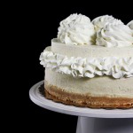 Banana Cream Cheese A close up, cropped photo of Banana Cream Cheesecake with layer of Bavarian Cream and decorated with Whipped Cream on a white cake stand with a black background.