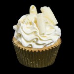 A photo of a White Chocolate Raspberry Cupcake frosted with Swiss Meringue Buttercream and decorated with chocolate curls and gold dust.