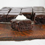 A photo of a slab of Espresso Chocolate Brownies with one removed, decorated with whipped cream and a chocolate covered espresso bean, and placed in front.