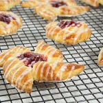 A photo of Cherry Danishes drizzled with icing cooling on a wire rack.