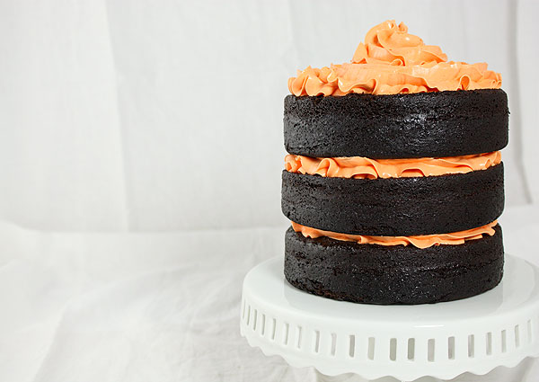 Grace's Sweet Life Chocolate Cake with Pumpkin A close up photo of a Chocolate Cake with Pumpkin decorated with orange-tinted Vanilla Bean-Swiss Meringue Buttercream taken with cake positioned to one side and displayed on a white cake stand.