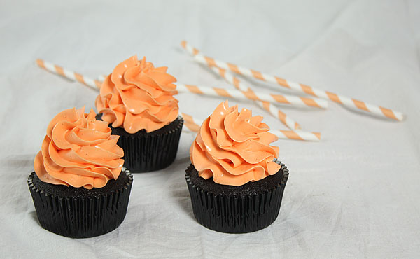 Grace's Sweet Life Chocolate Pumpkin Spice Cake A photo taken looking down on three mini Chocolate Pumpkin Spice Cakes decorated with orange-tinted Swiss Meringue Buttercream displayed with orange and white striped straws.