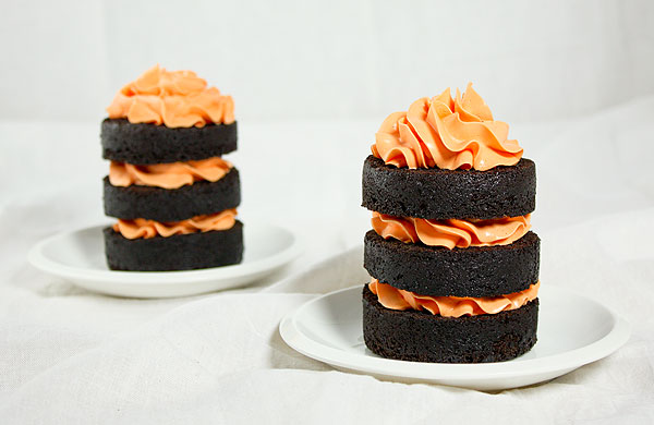 Grace's Sweet Life Mini Chocolate Pumpkin Cakes A photo of two Mini Chocolate Pumpkin Cakes layered with orange-tinted Swiss Meringue Buttercream with Vanilla Bean displayed on white dessert plates.