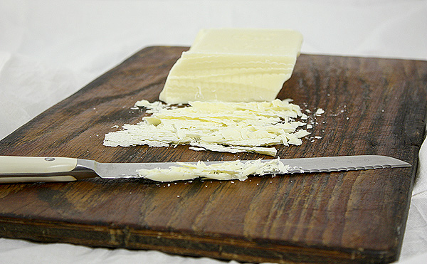 Vanilla Bean Pudding mise en place, block of white chocolate, displayed on a dark wooden board with serrated knife.
