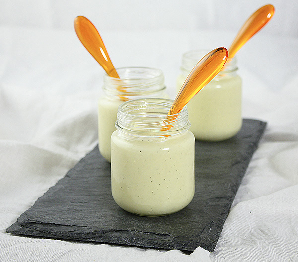 A photo of three Vanilla Bean Pudding desserts in glass jars displayed with orange dessert spoons.