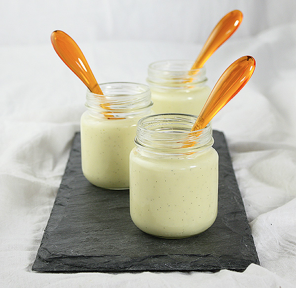Homemade Vanilla Pudding in glass jars displayed on rectangular-shaped slate board with orange acrylic dessert spoons.