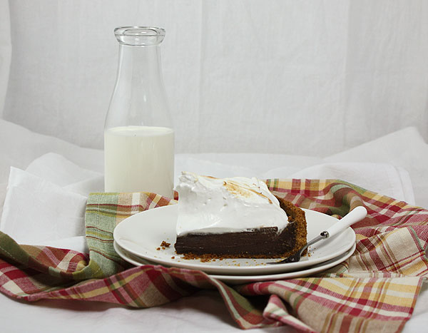 A photo of a slice of S mores Pie displayed on multi-colour cloth napkin with jug of milk.