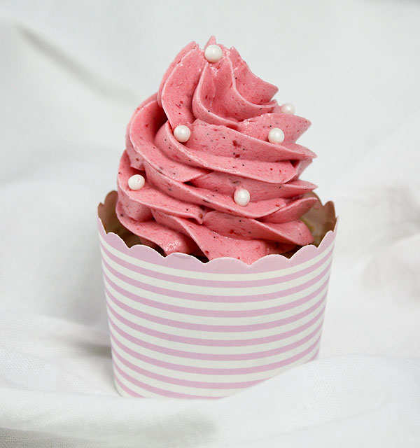 Close up photo of a Strawberry Cupcake with Pink Strawberry Meringue Buttercream displayed in pink striped cupcake cup and decorated with white sugar pearls.