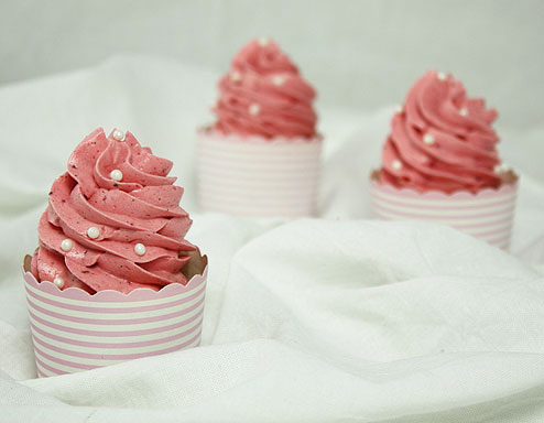 A photo a Strawberry Cupcake with two additional cupcakes set in behind and blurred.