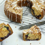 A photo taken looking down on a Blueberry-Almond Streusel Coffee Cake with a few cut slices displayed on wire rack place on marble pastry board..
