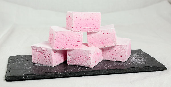 A close up photo of Gourmet Strawberry Marshmallows stacked on rectangular shaped black slate board.