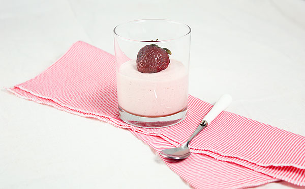 A photo of strawberry mousse in a glass garnished with fresh strawberry displayed on a pink and white striped napkin.