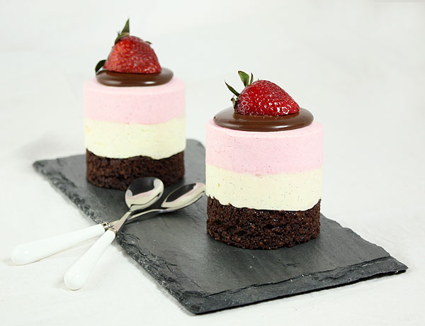 A photo of two Mini Neapolitan Mousse Cakes displayed with desserts spoons on slate board.