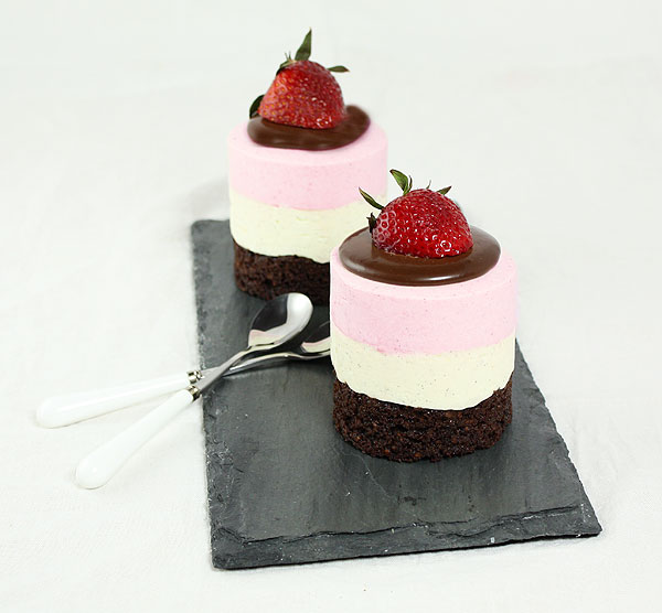 A photo taken looking down on two Neapolitan Layer Mousse Cakes garnished with fresh strawberries.