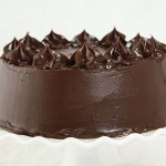 Close up photo of Hazelnut and Orange Chocolate Cake layered with Orange Chocolate Ganache displayed on white cake stand.