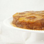A cropped and close up photo of Pineapple Upside-Down Cake displayed on white cake stand.