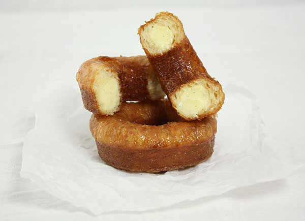 Photo of two Croissant Doughnuts, one cut in half exposing the many interior layers.
