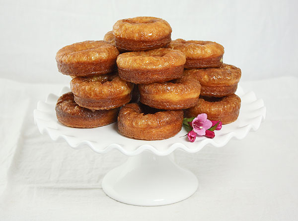Photo of Vanilla Bean Cream Filled Croissant Doughnuts displayed with pink flowers on white cake stand.