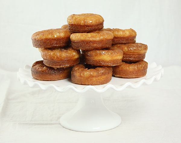 Photo of Honey Dipped Croissant Doughnuts piled high on a white cake stand.