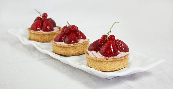 Close up photo of three Berry Cheesecake Tarts displayed in a row on white rectangle shaped white serving dish.