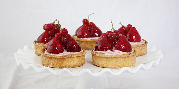 Close up photo of Cheesecake Tarts with Strawberries displayed on white cake stand.
