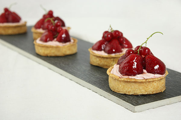 Photo of five Strawberry Cheesecake Tarts displayed in a row on rectangle shaped black tile.