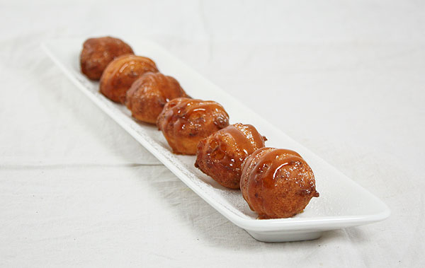 Photo of Sweet Italian Fritters drizzled with caramel sauce displayed in a row on white rectangle shaped serving dish.