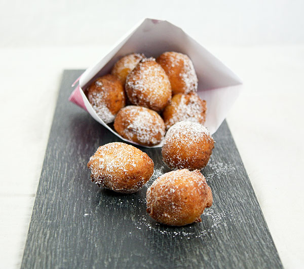 Photo of Ricotta Beignets tumbling our of paper cone onto slate board.