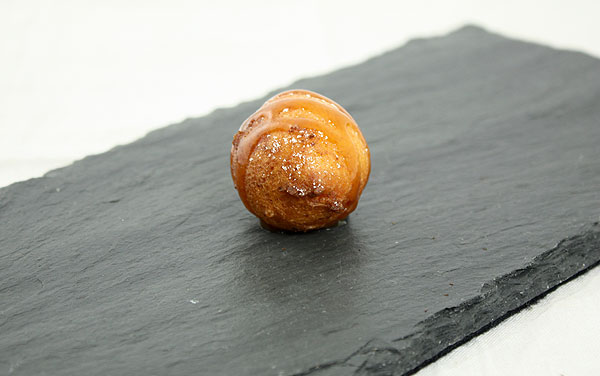 Close up photo of one Ricotta Fritter drizzled with Butter-Rum Caramel Sauce on slate board.