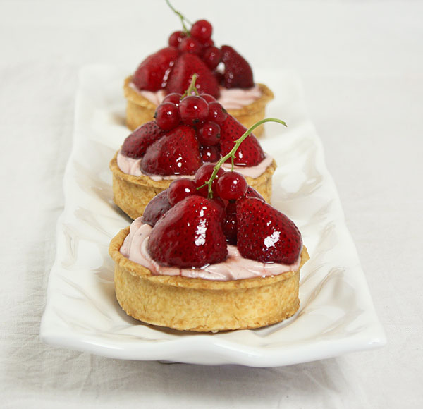 Close up photo of Strawberry Tarts displayed in a row, one behind the other on white rectangle shaped, textured white serving dish.