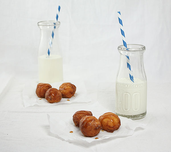Photo of Italian Sweet fritters displayed on parchment squares with jugs of milk.