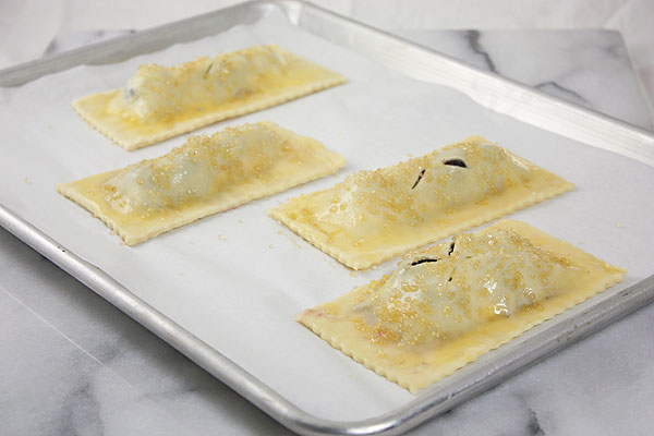 Berry Hand Pies on baking paper lined rimmed baking sheet ready for baking.