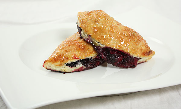 A photo of two moon-shaped mini Blackberry Pies on white dessert dish.