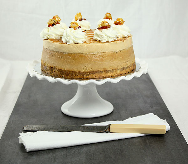 Photo of Dulce de Leche Cheesecake on white cake stand displayed with cake knife.