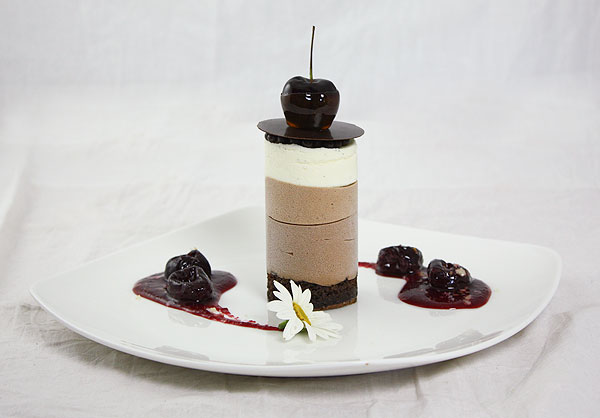 Mini Triple Chocolate Mousse Cake with Cherry Sauce on white dessert dish.