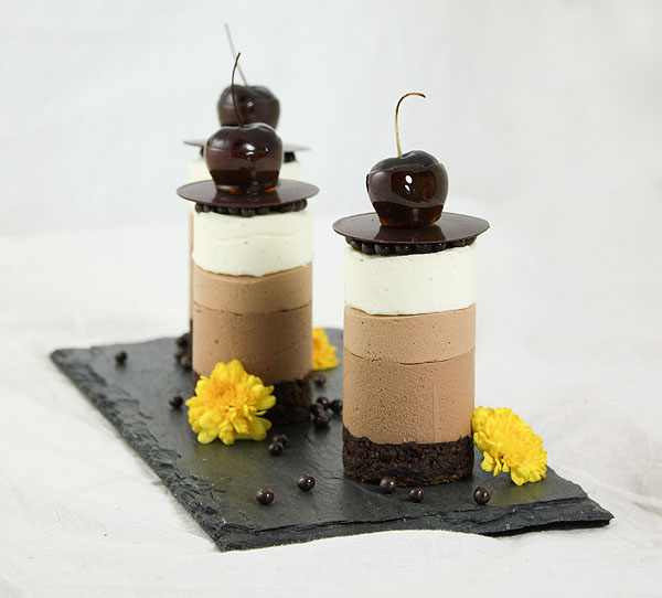 Mini Triple Chocolate Mousse Cakes decorated with Crispearls, Chocolate Disc, Caramel Dipped Cherries and Edible Flowers displayed on black slate board.