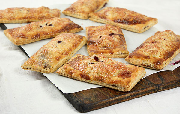 A photo of freshly baked blackberry Hand Pies displayed on dark wooden board lined with baking paper.