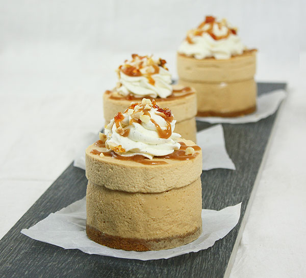 Photo of three Mini Dulce de Leche Cheesecakes displayed in a row, one behind the other, on parchment squares and displayed on rectangle shaped black tile.