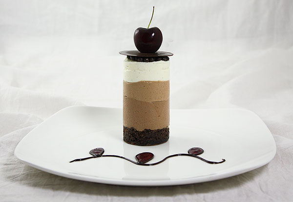 Mini Triple Chocolate Mousse Cake plated on white dessert dish decorated with chocolate and cherry purée.