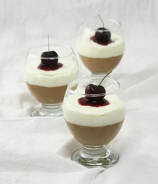 Three Triple Chocolate Mousse Desserts displayed in glasses and topped with Cherry Sauce and fresh cherries.