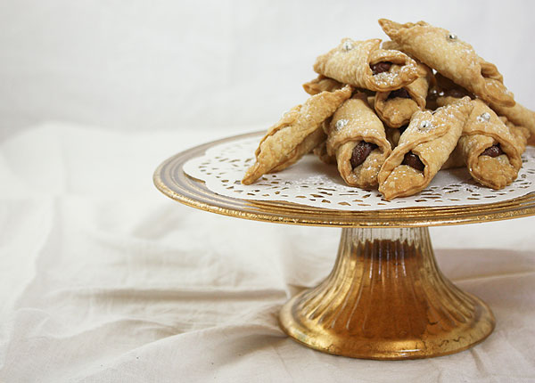 Cropped photo of Nutella filled Italian cookies stacked on a gold cake stand lined with white doilie.