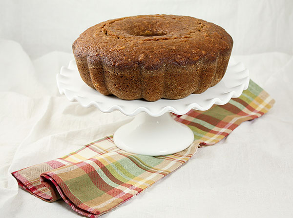 Photo taken looking down on Pear Bread displayed on white cake stand with multi coloured cloth napkin.